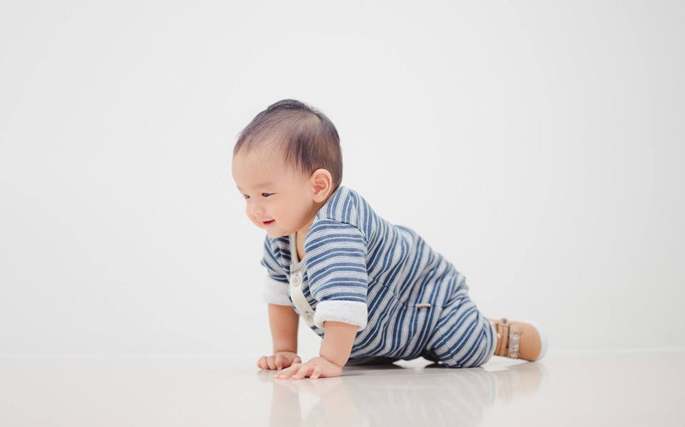 ทารกวัย 6 เดือนกำลังคลานบนพื้น สวมชุดลายทางสีฟ้าขาว